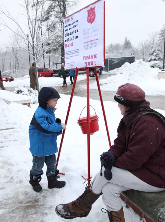 Four-year-old Austin Backer-Verbits puts his donation for Haiti relief into a Salvation Army bucket as volunteer Melissa Marteney looks on.