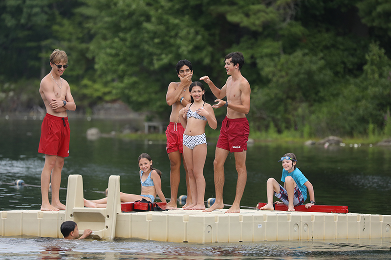 From left: Jackson Whitley, Jeremy Brown (in water), Julianno Liuzzi, Shane Trabulsi, Gianna Baer, Shea Van Cleef, and Jack Hogan hang out on a raft during swimming lessons at the town beach, Aug. 5. (Photo by Lisa Aciukewicz)